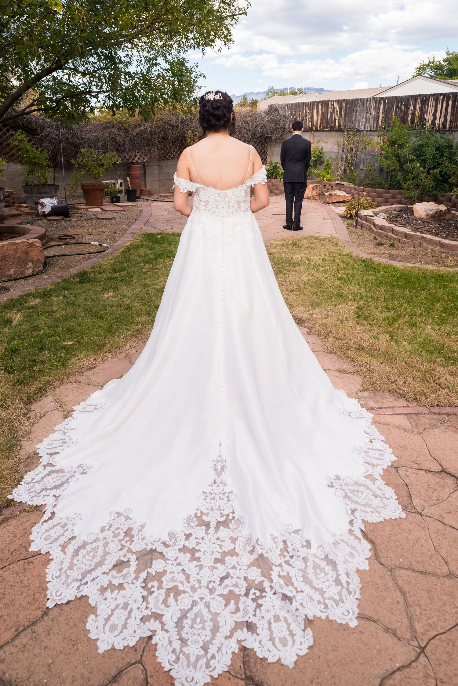 Wedding dress with intricate lace train displayed in garden setting.