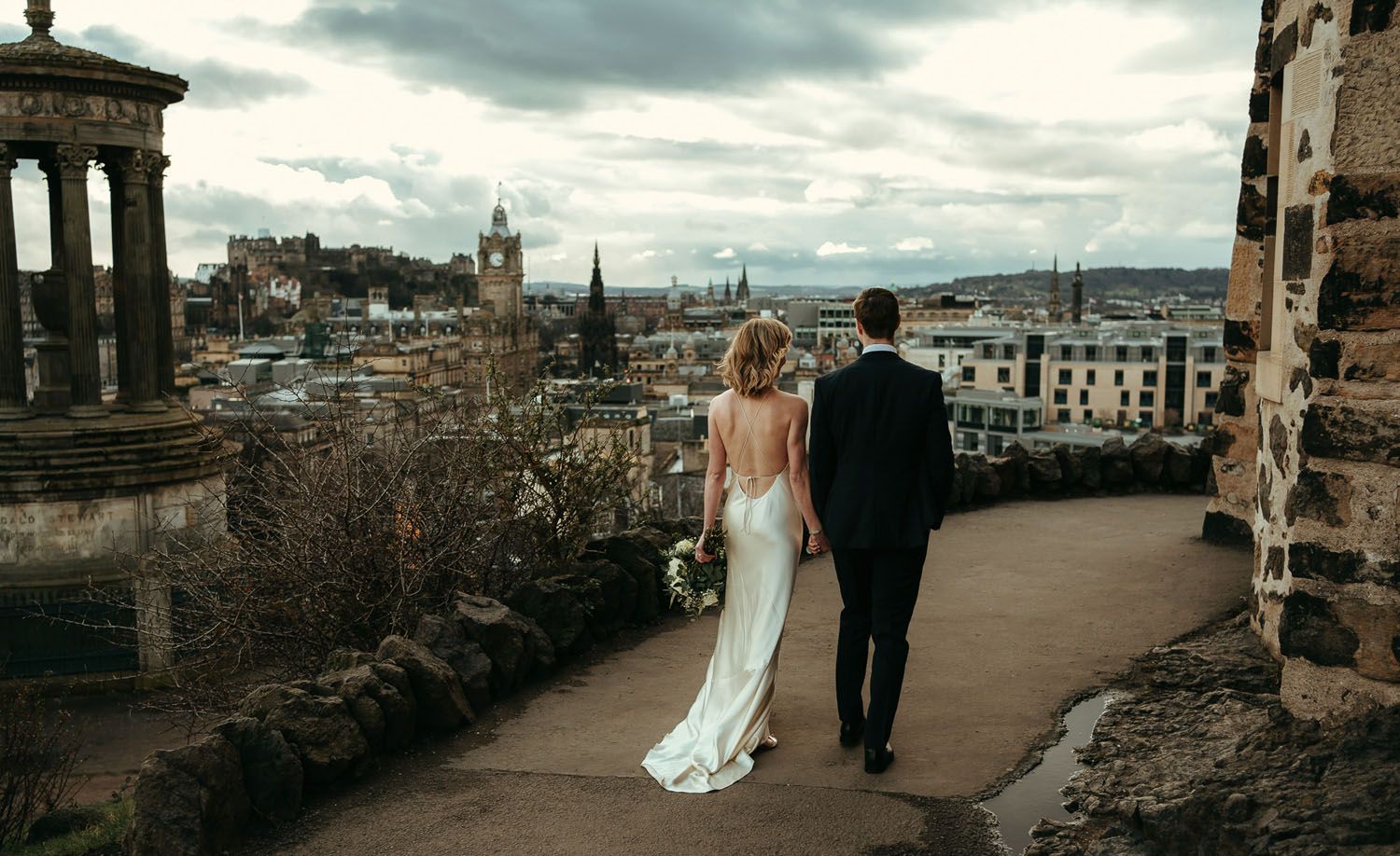 Bride and groom walking hand in hand on a charming cobblestone street lined with stone buildings on their wedding day.