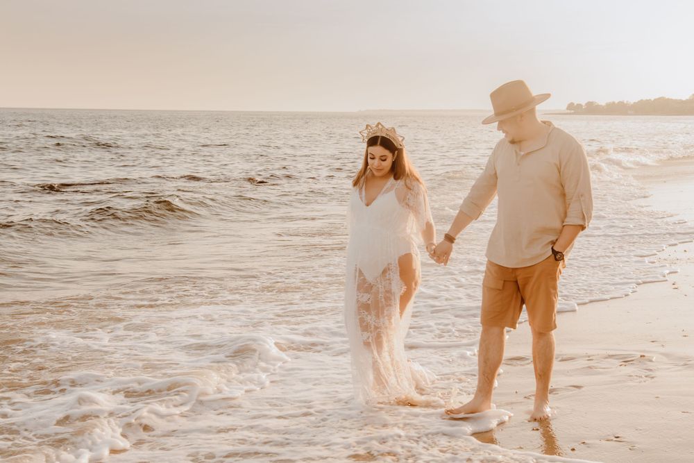 A couple walks hand in hand along a beach shoreline at sunset.