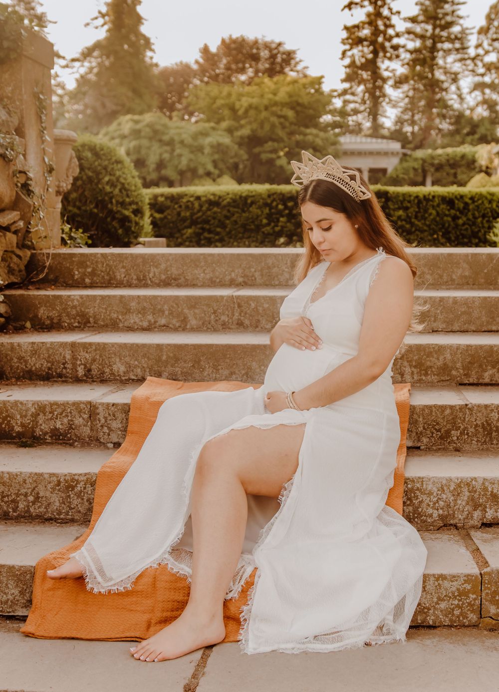 A dreamy maternity pose on stone steps surrounded by greenery at sunset.