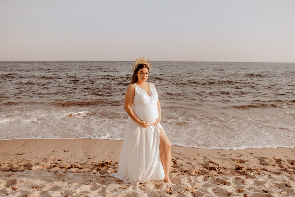 A white flowing dress against the backdrop of waves on a sandy beach at sunset.