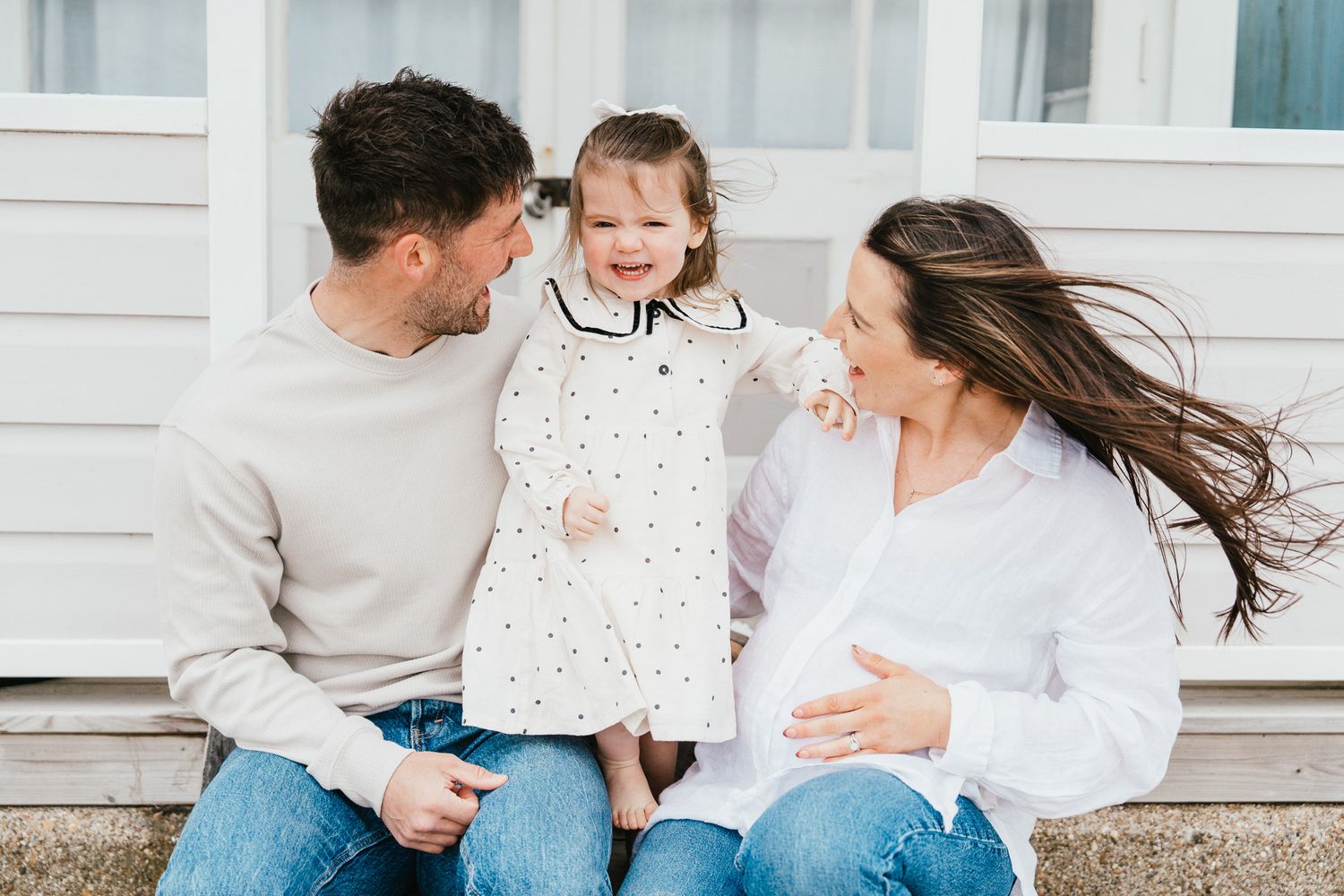 Family sitting outside white building sharing joyful moment with young child.