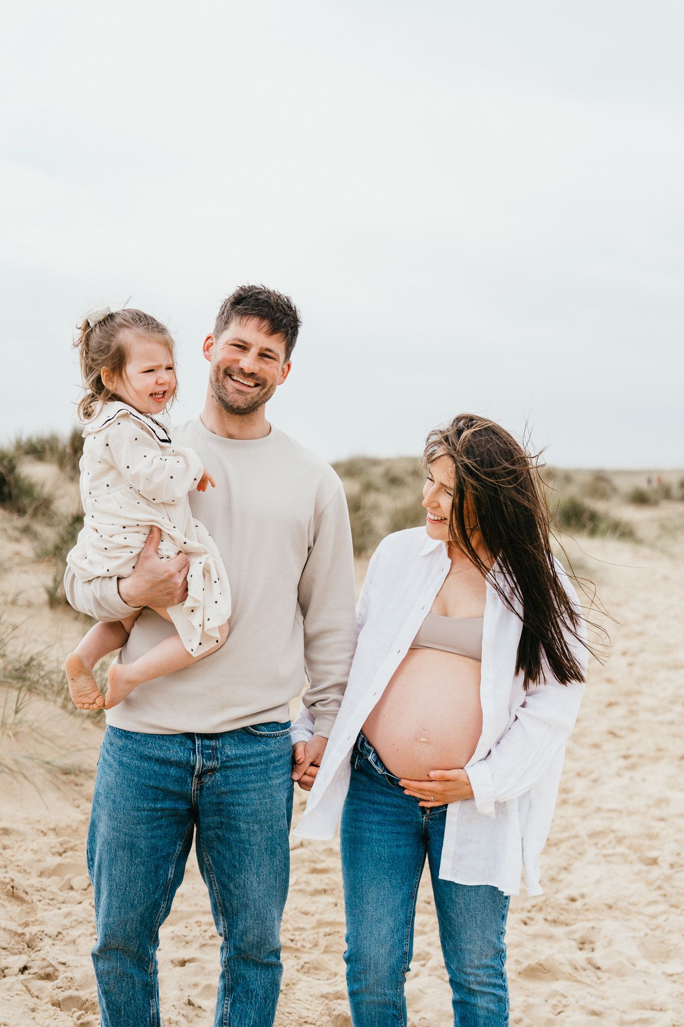 Family enjoying a sunny day at the beach while expecting a new addition.