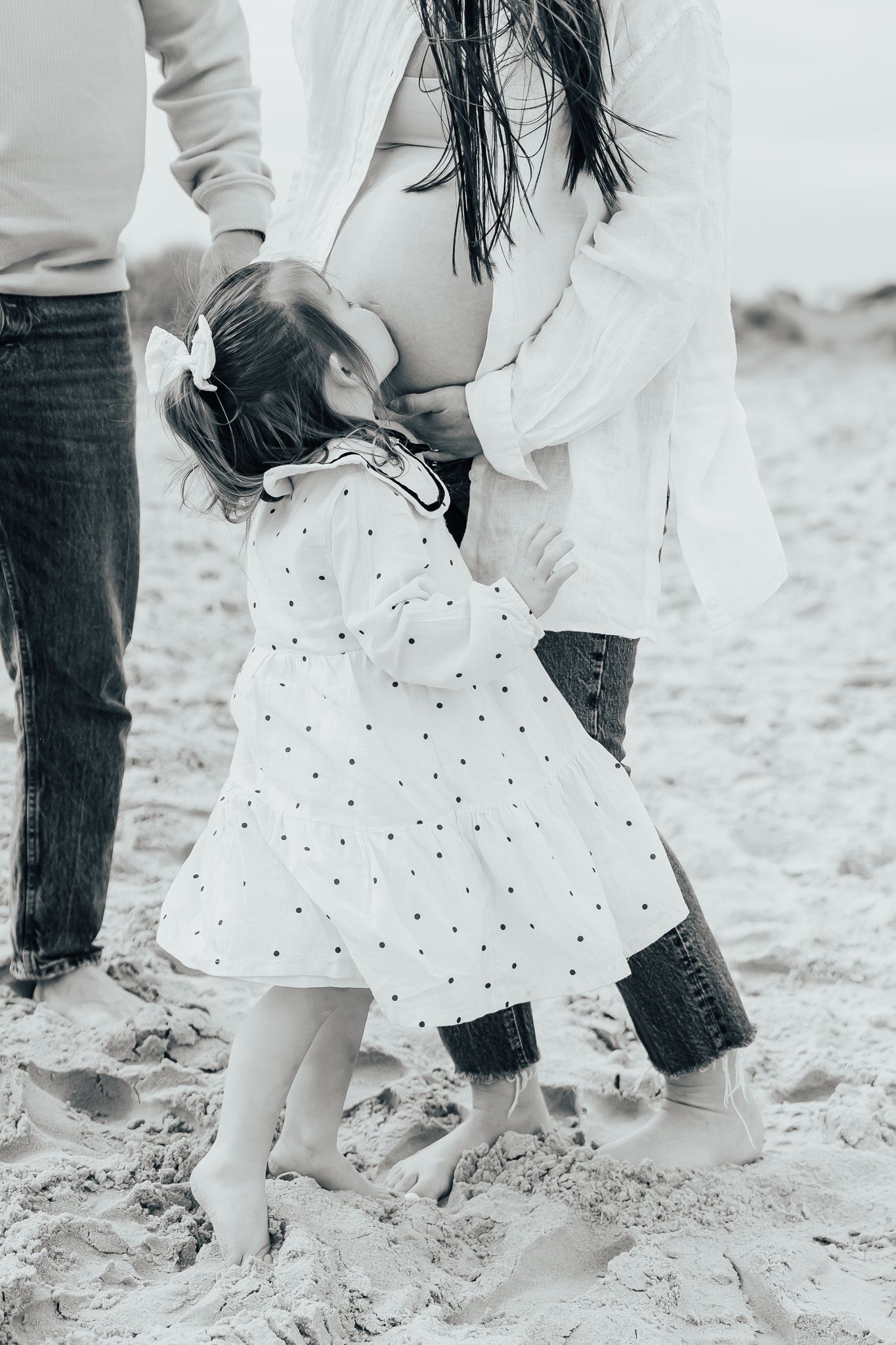 Little one in polka dot dress kissing mums baby bump.