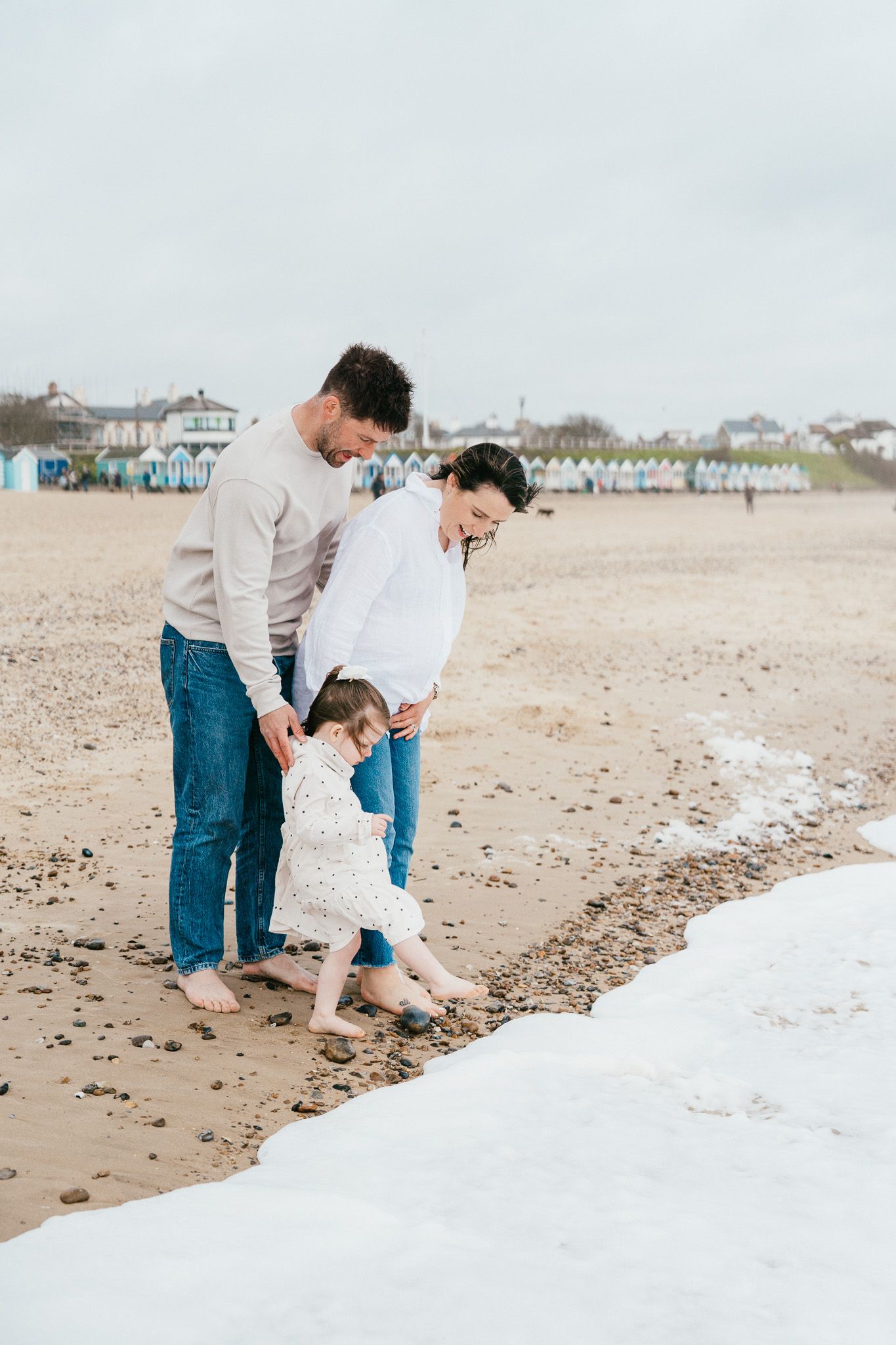 Family exploring beach shoreline together near beach huts.