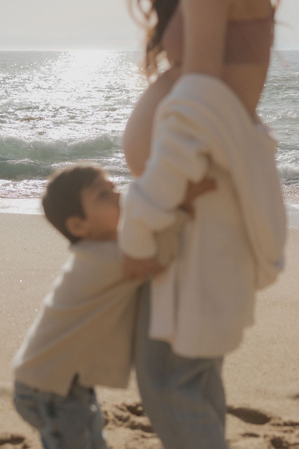 A touching beachside moment between mother and child with ocean waves in background.