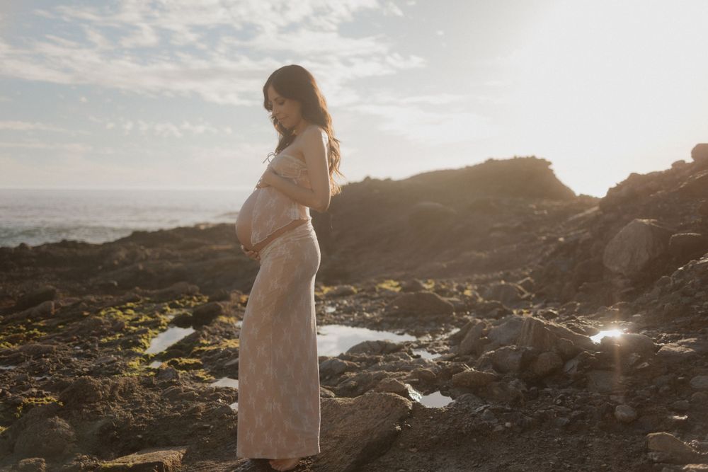 A figure in white stands against rocky coastal scenery at sunset.