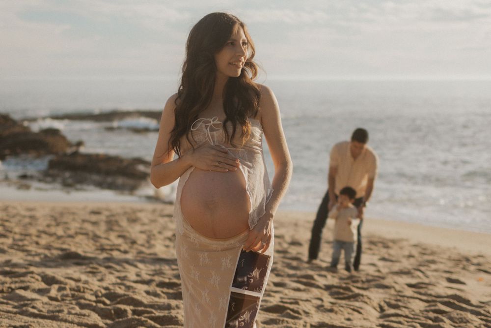 A maternity photo shoot on a scenic beach with waves and rocks in the background.