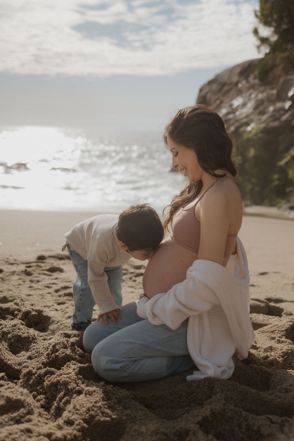 Maternity beach photo with child exploring sand beside pregnant woman.