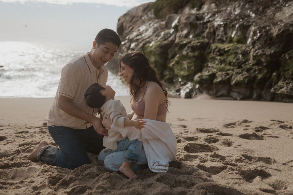 Family shares tender moment on sandy beach during maternity photoshoot.