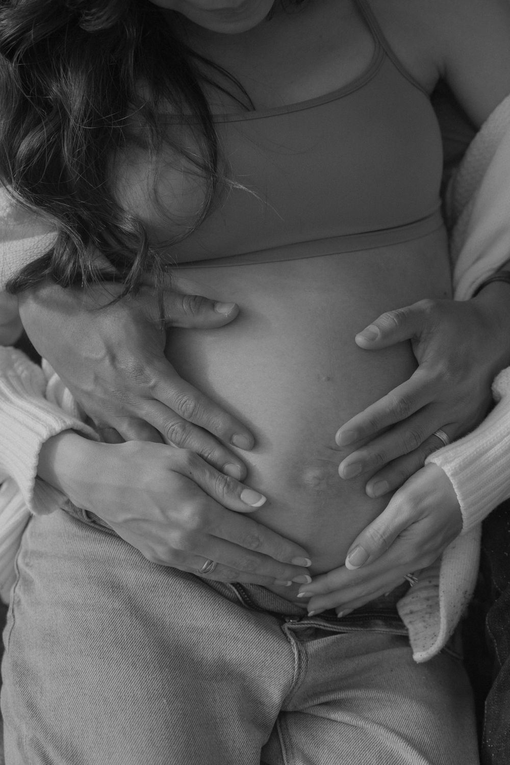 A black and white close-up of hands tenderly cradling a pregnant belly.