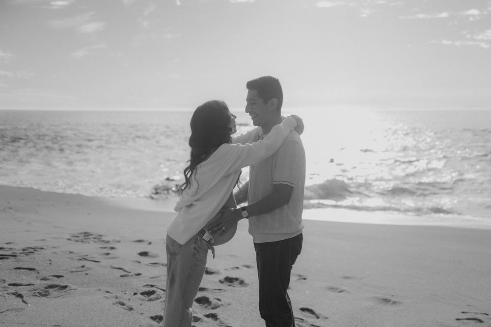 A couple embraces on a sunlit beach in black and white photography.