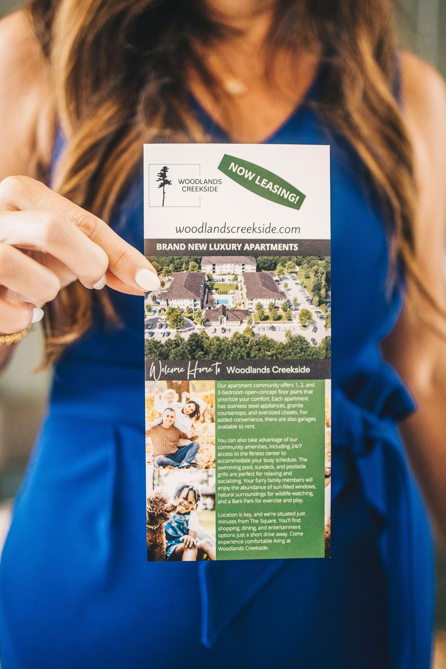 Woman in blue dress holding Woodlands Creekside luxury apartments brochure.