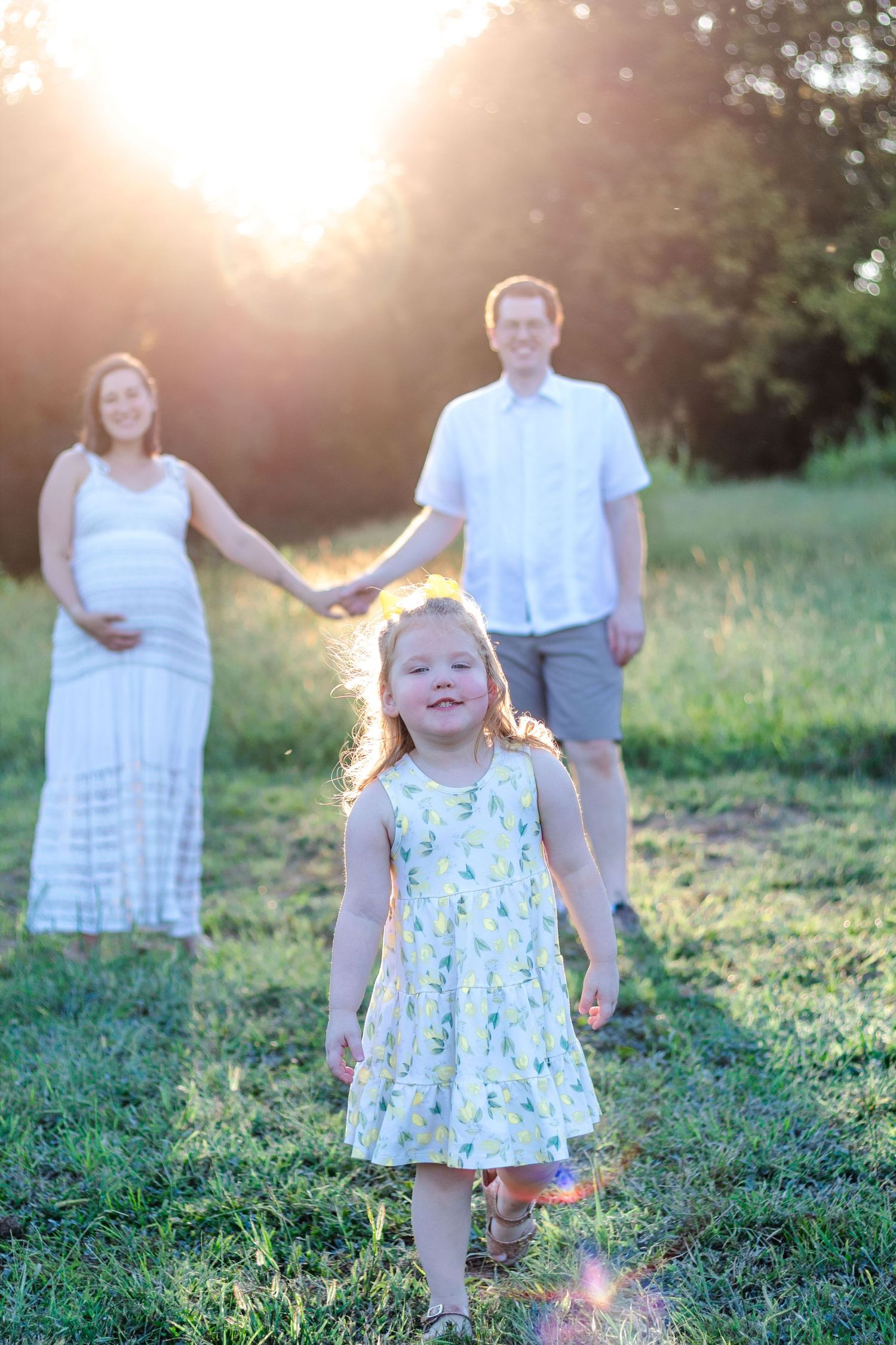 Mom and dad standing in background, toddler closer to camera smiling