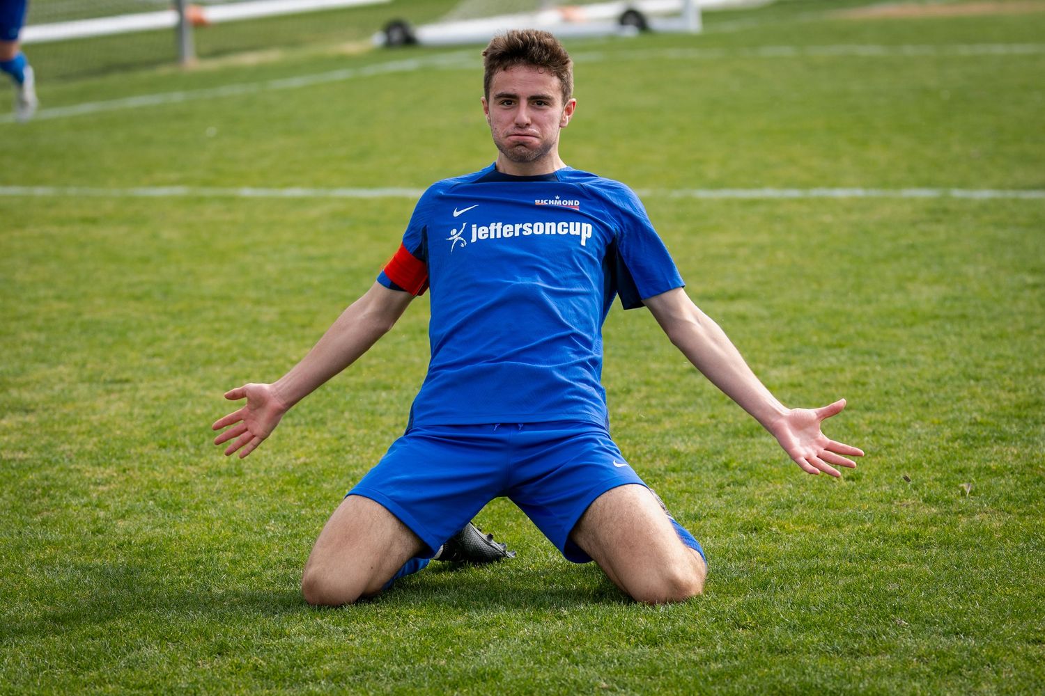 Soccer players in blue uniforms stretching on grass field during practice.