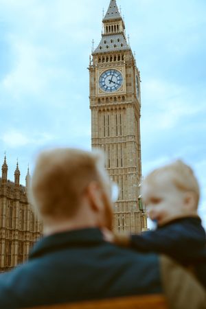 A father holding his young child, seen from behind, with Big Ben towering in the background during a family trip to London.