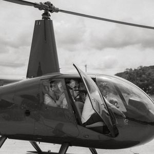 Black and white photo of a smiling mother wearing aviation headsets waving from inside a helicopter next to her excited toddler.