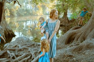 A mother and her children exploring the scenic, tree-lined riverbank of the Guadalupe River in Central Texas.