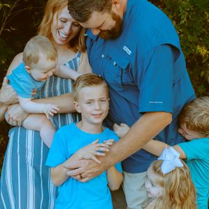 A close-up family portrait of a couple smiling and hugging their four young children during an outdoor lifestyle photo shoot.