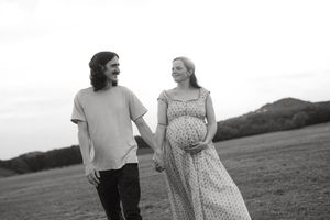 Black and white maternity photo of a couple holding hands and walking through a Central Texas field.