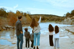 A family seen from behind as a woman points out across the Blanco River during a photo session in Wimberley, Texas.