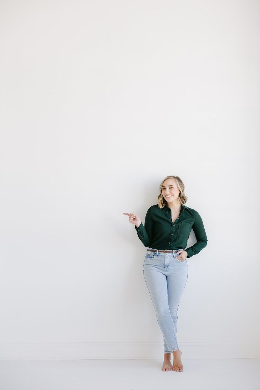 Branding portrait against white wall, person wearing green top and light denim, pointing playfully.