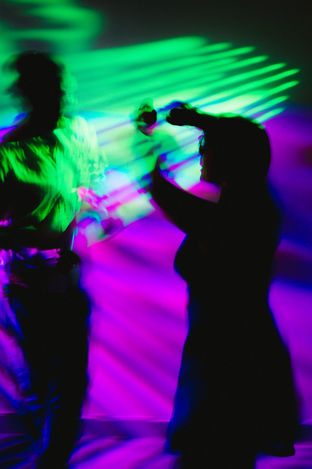 Silhouettes of two people dancing under vibrant neon green and purple lights at a nightclub party.