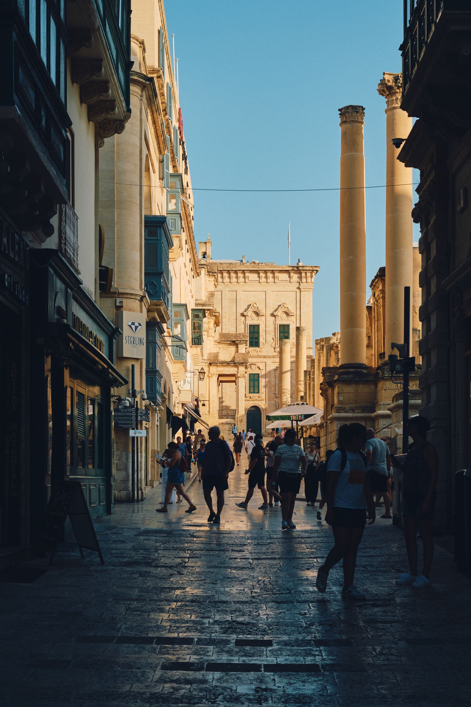 Historic stone street with tall columns and architecture in Malta's old town during golden hour.