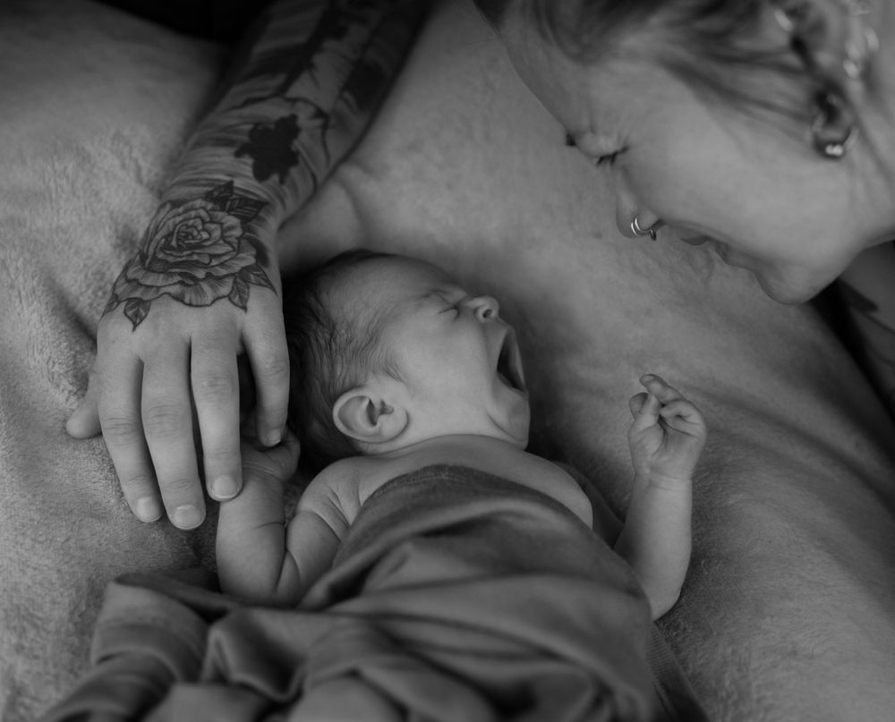 Black and white photo of sleeping infant with tattooed hand gently resting nearby.