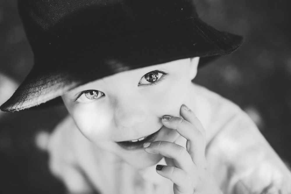 Black and white photo of a child in a hat with a thoughtful expression touching their face.