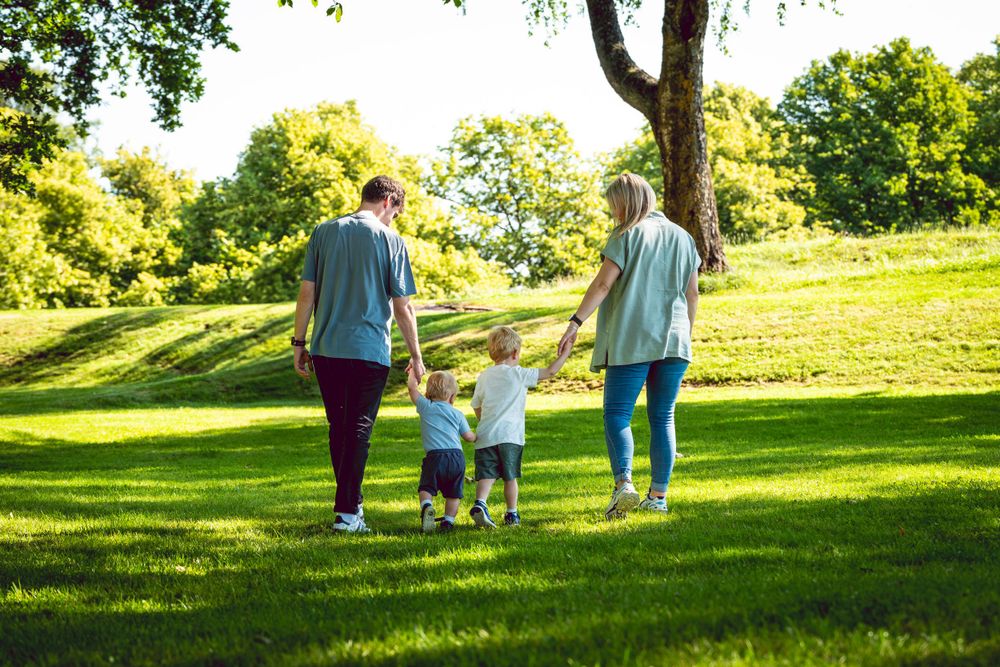 A family walks together holding hands on a grassy hill during a sunny day.