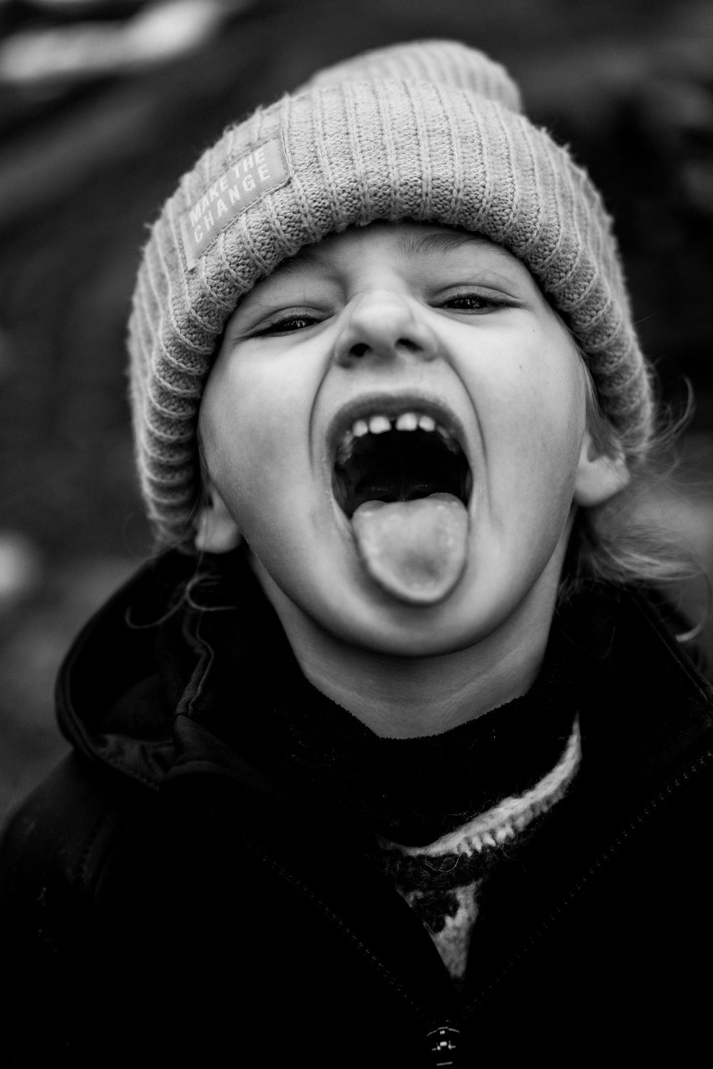 Black and white photo of a young child wearing a knit beanie, sticking out tongue with mouth wide open.