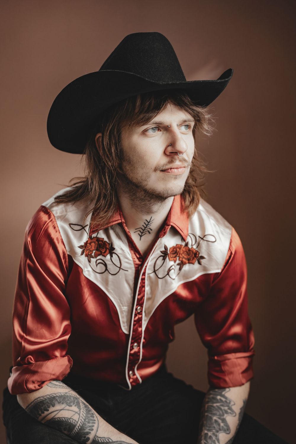 Four artistic portrait photographs showing a person in a red button-up shirt and black cowboy hat against a brown backdrop.