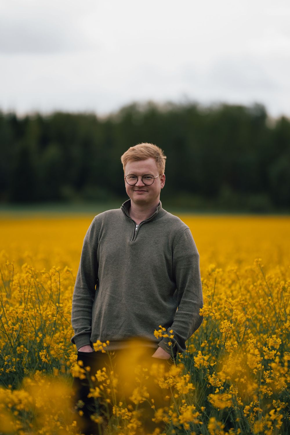 Person with a sweater stands in vibrant yellow canola field during a cloudy day.