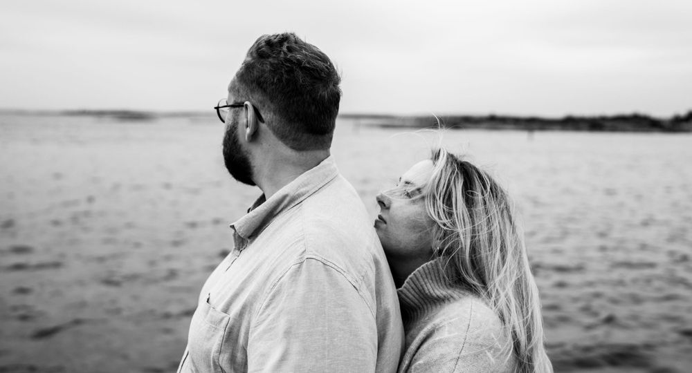 Romantic black and white portrait of couple embracing by the ocean.