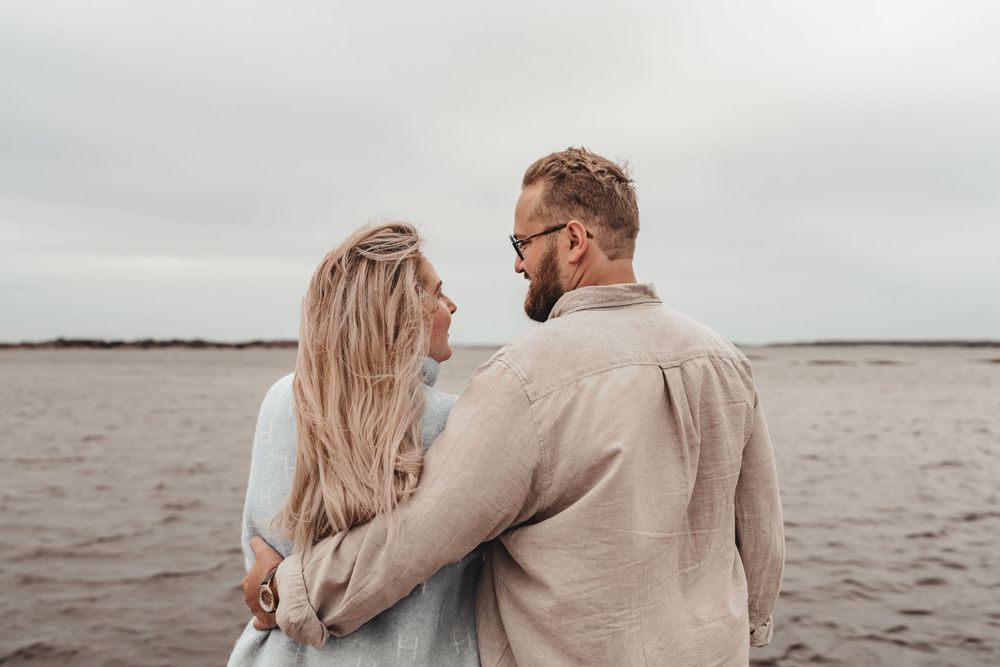 Couple in light colored clothing sharing intimate moment on beach.