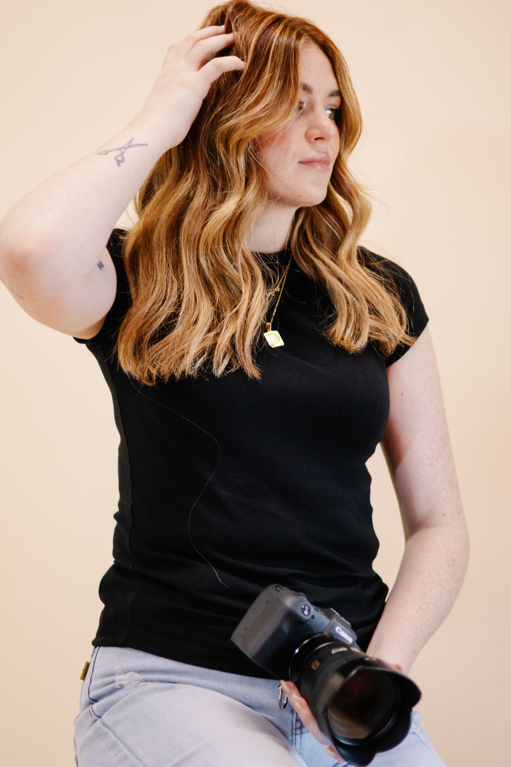 Person in black shirt and jeans posing casually against beige wall.