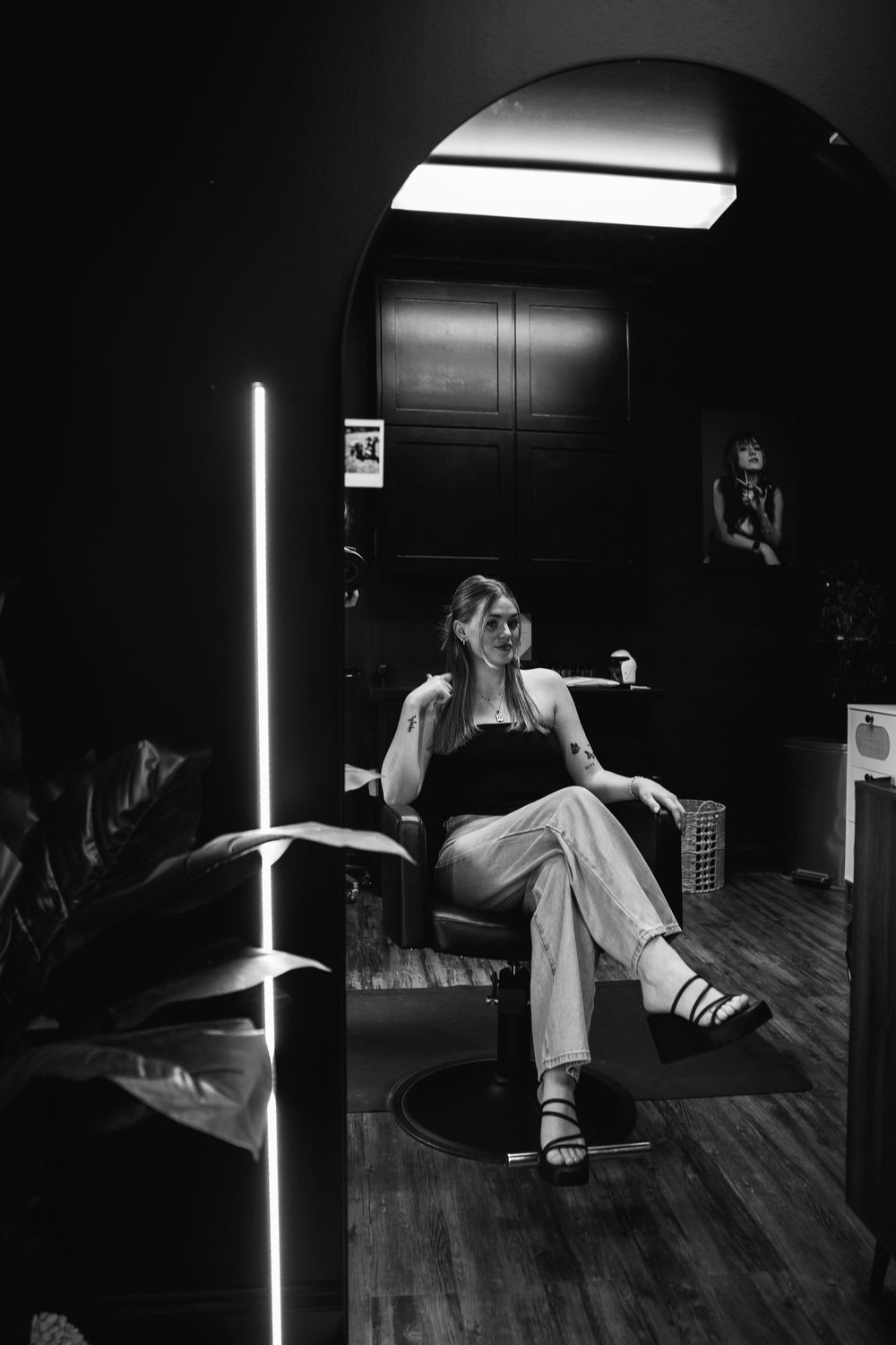 Dramatic black and white photo of person seated in dark studio with vertical light fixture.