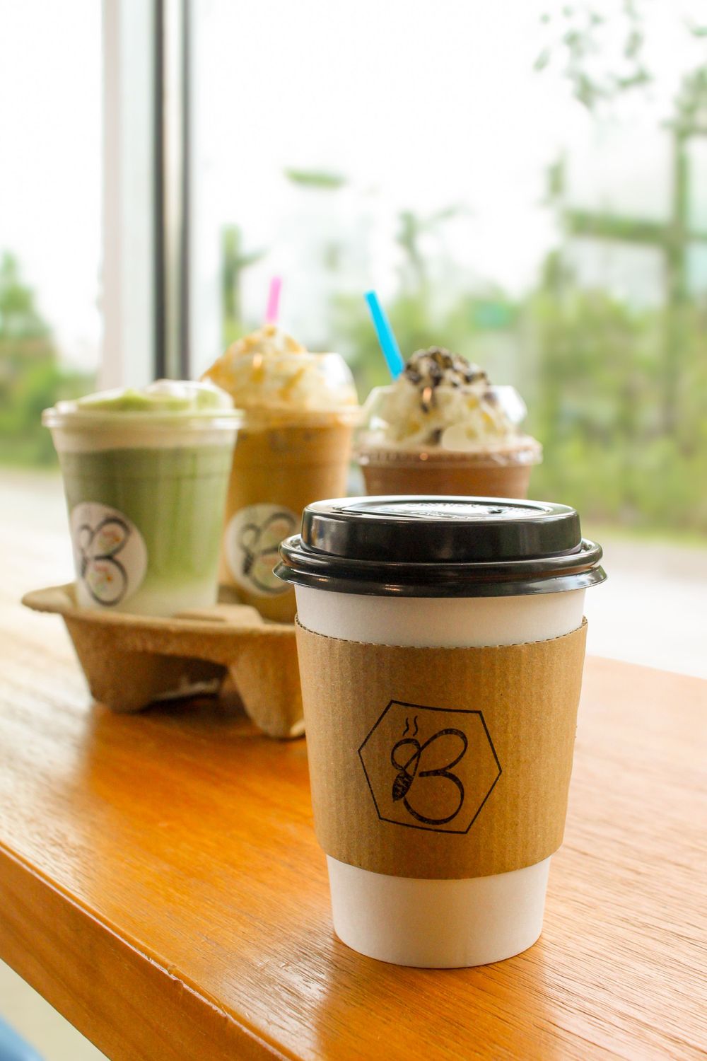 Various coffee drinks including hot and frozen beverages with whipped cream displayed on wooden counter with branded sleeves.