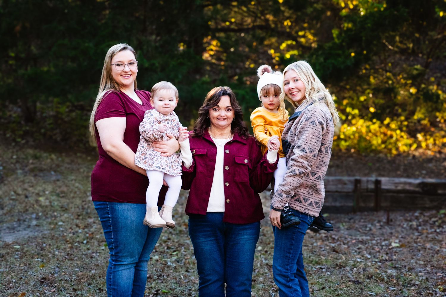 Group portrait of five people wearing burgundy and neutral tones against autumn foliage.