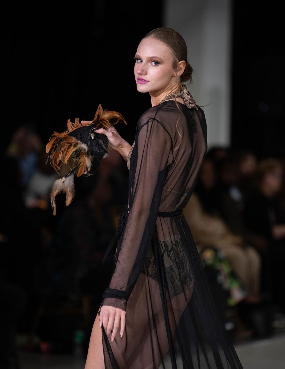 Model showcases sheer brown gown with dramatic sleeves on fashion runway.