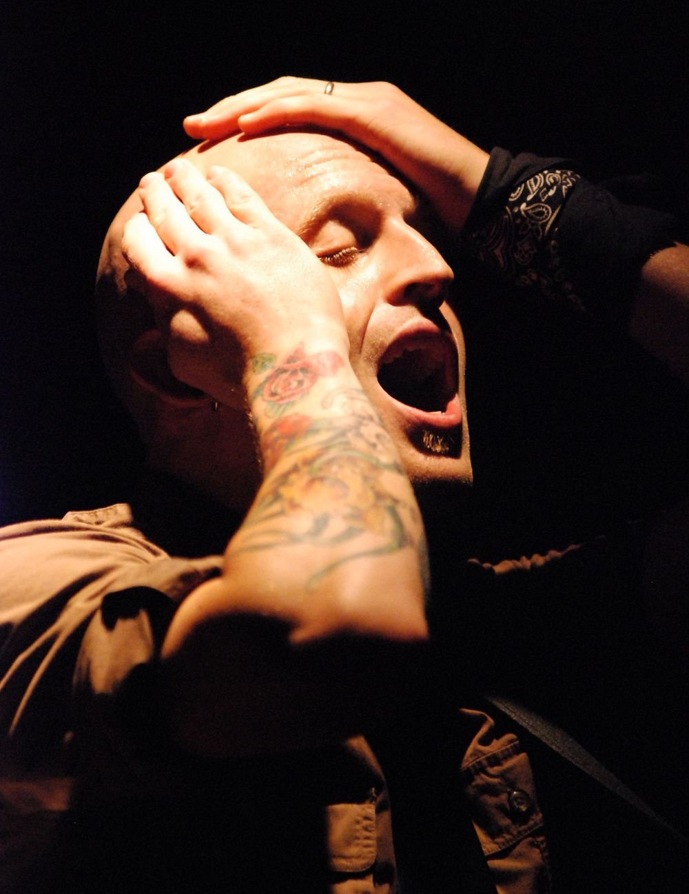 Fred Schaffer Music singing with hands on bald head lit by stage lights
