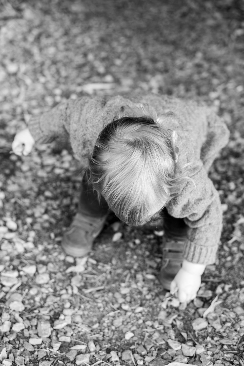 Small child in grey sweater bending down to examine something on the ground.