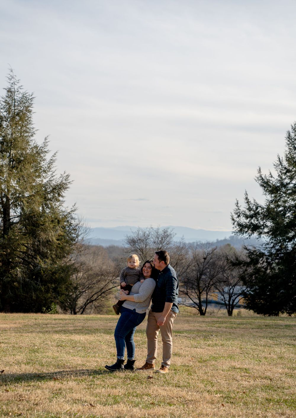 Three people relax together on a grassy hillside with mountains in the background.