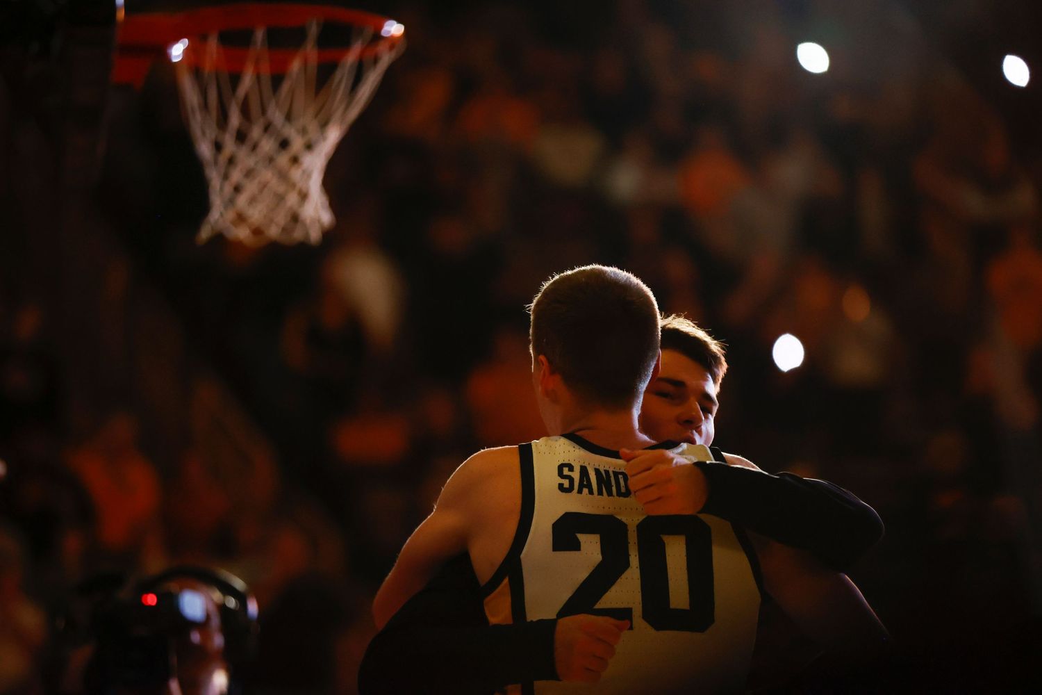 Silhouette of basketball players against dark arena lighting during game.