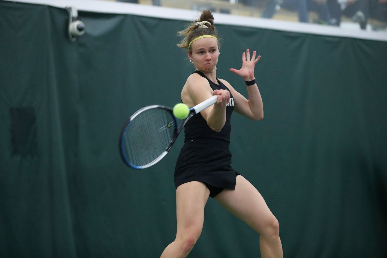 Tennis player hits forehand shot during indoor match.