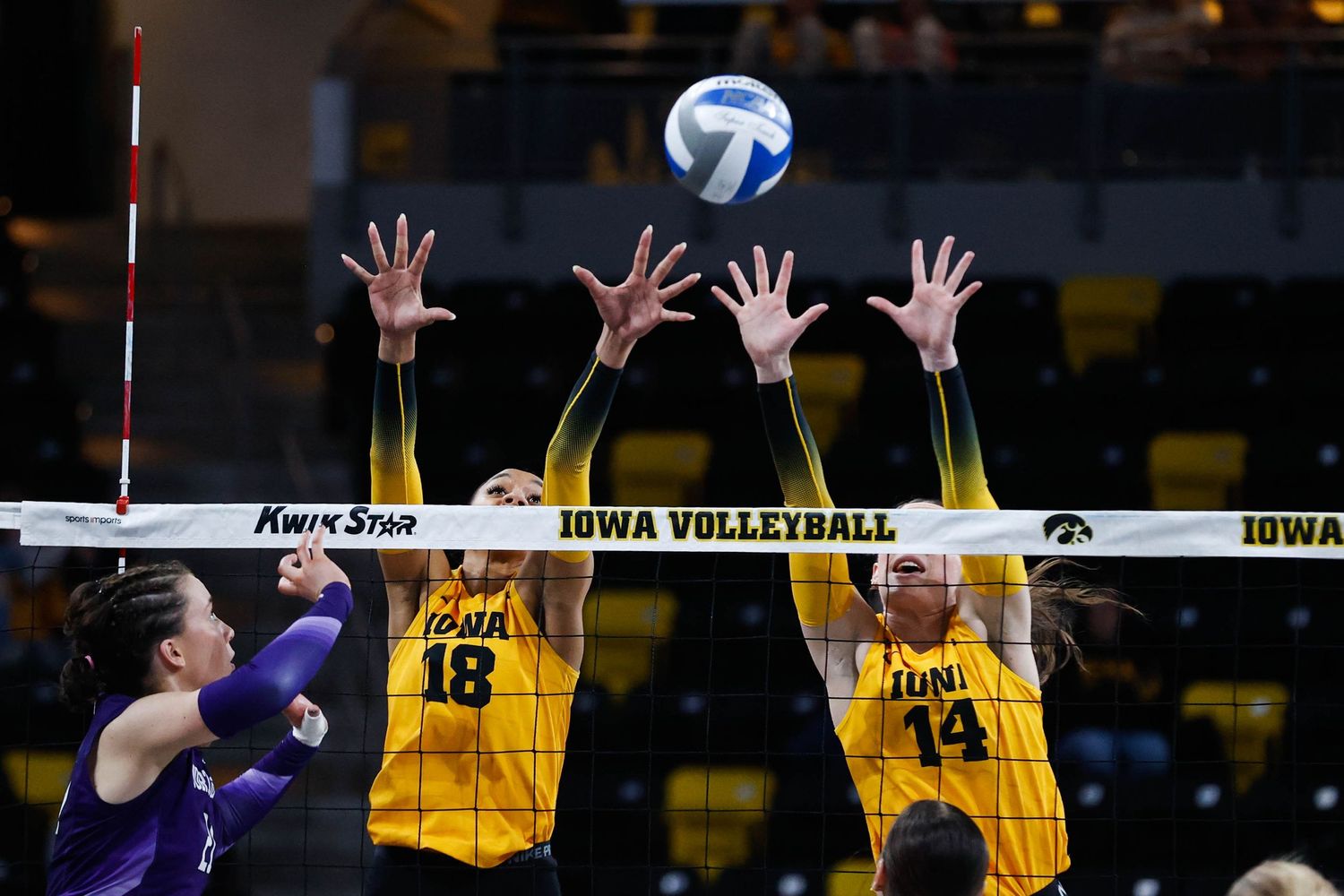 Two volleyball players jump to block a spike during an Iowa volleyball match.