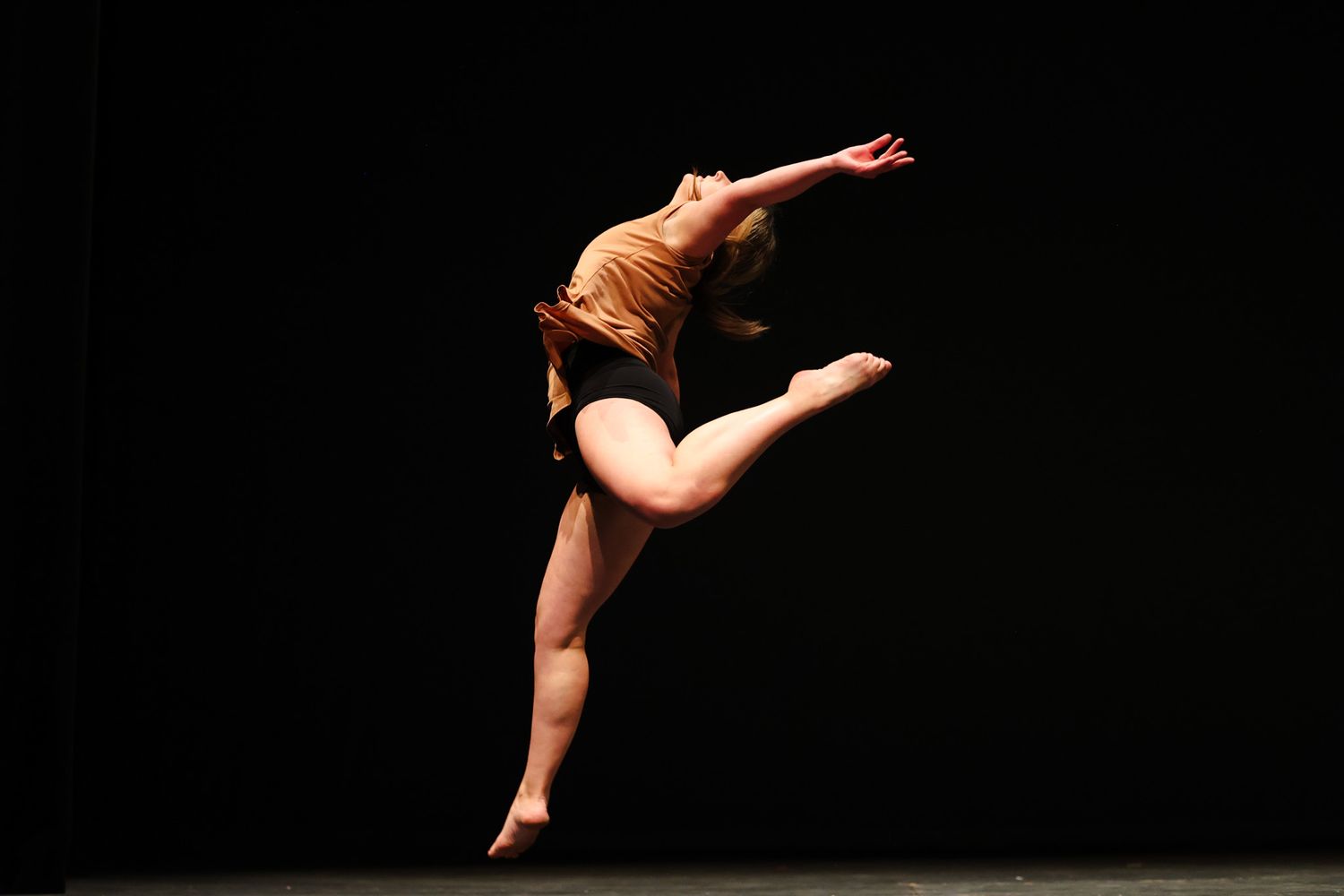 Dancer performs graceful arabesque pose against dark background.
