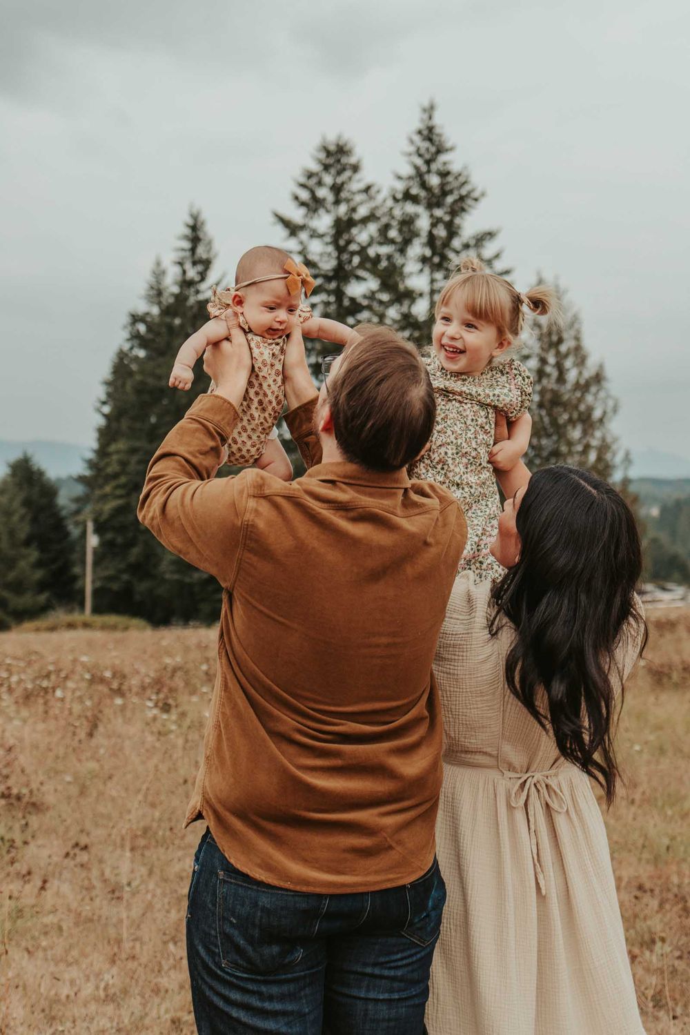 mom and dad lifting their daughters playfully into the air in a big open field