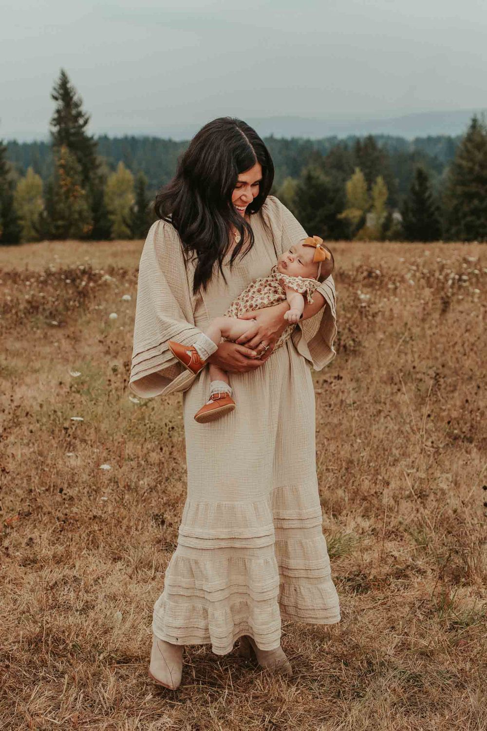 mom in cream dress in a grassy field holding her new baby girl